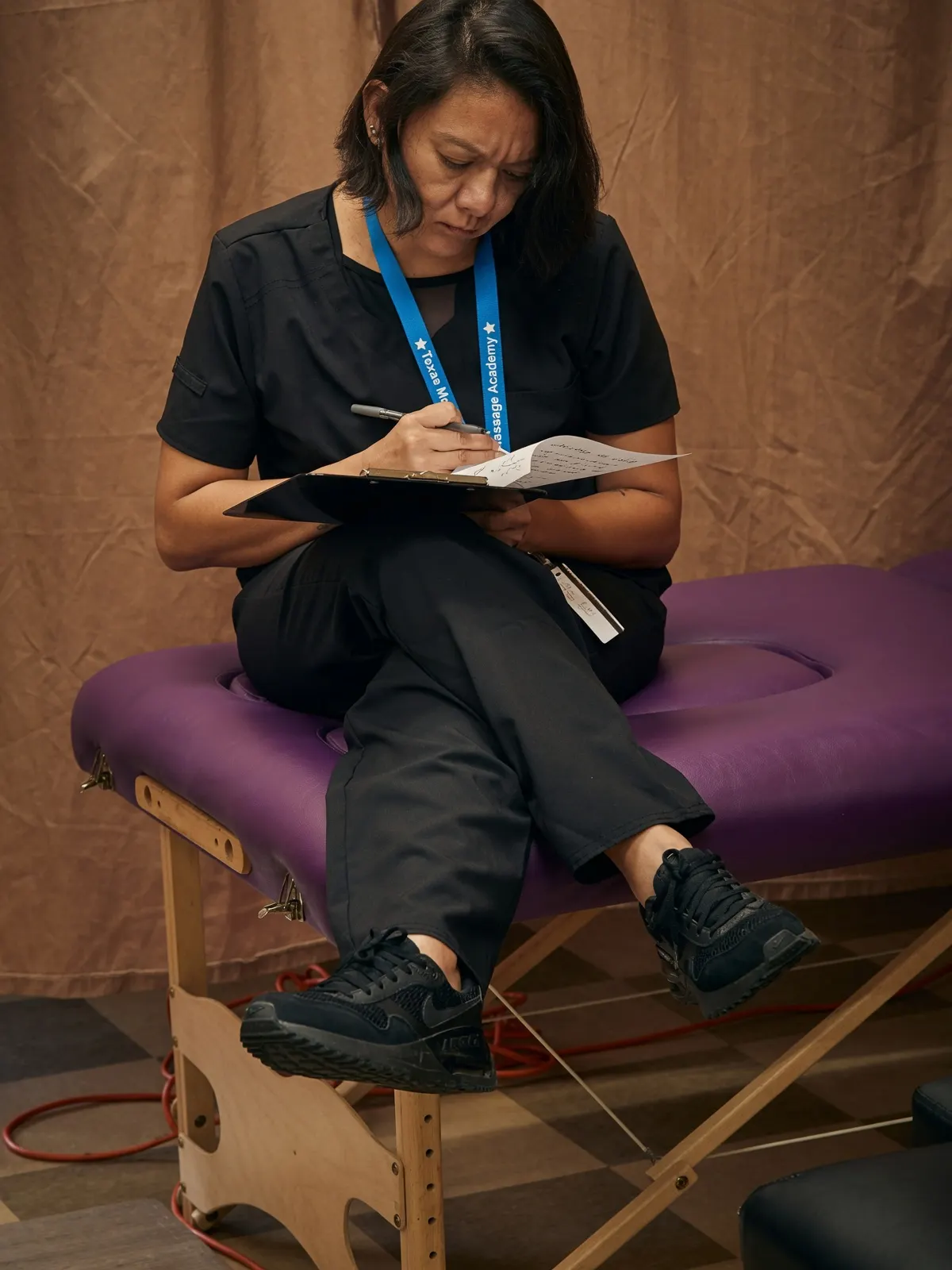 Female student writing clipboard notes on massage table — Texas Massage Academy, Brownwood TX
