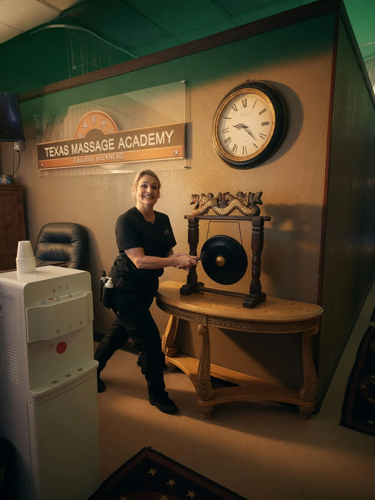Instructor ringing the gong beneath the Texas Massage Academy sign