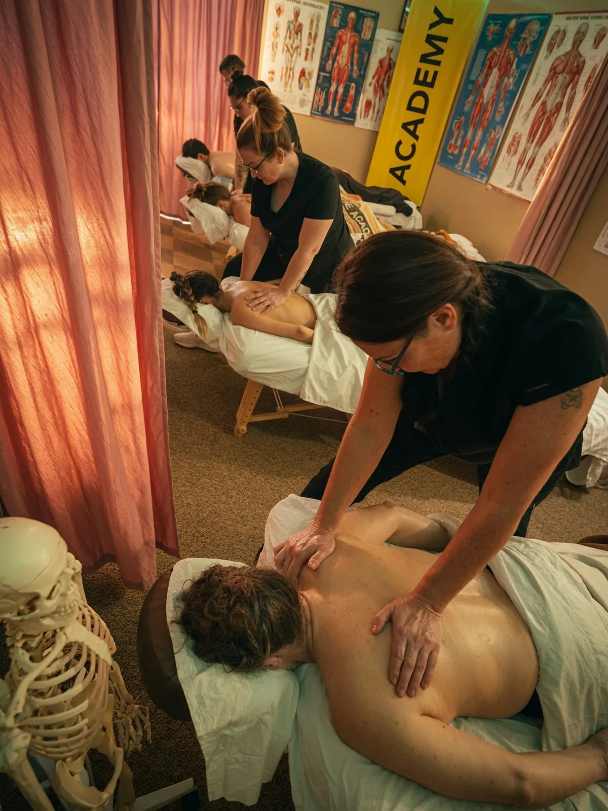 Students giving massages on a row of tables beside a skeleton and muscle charts