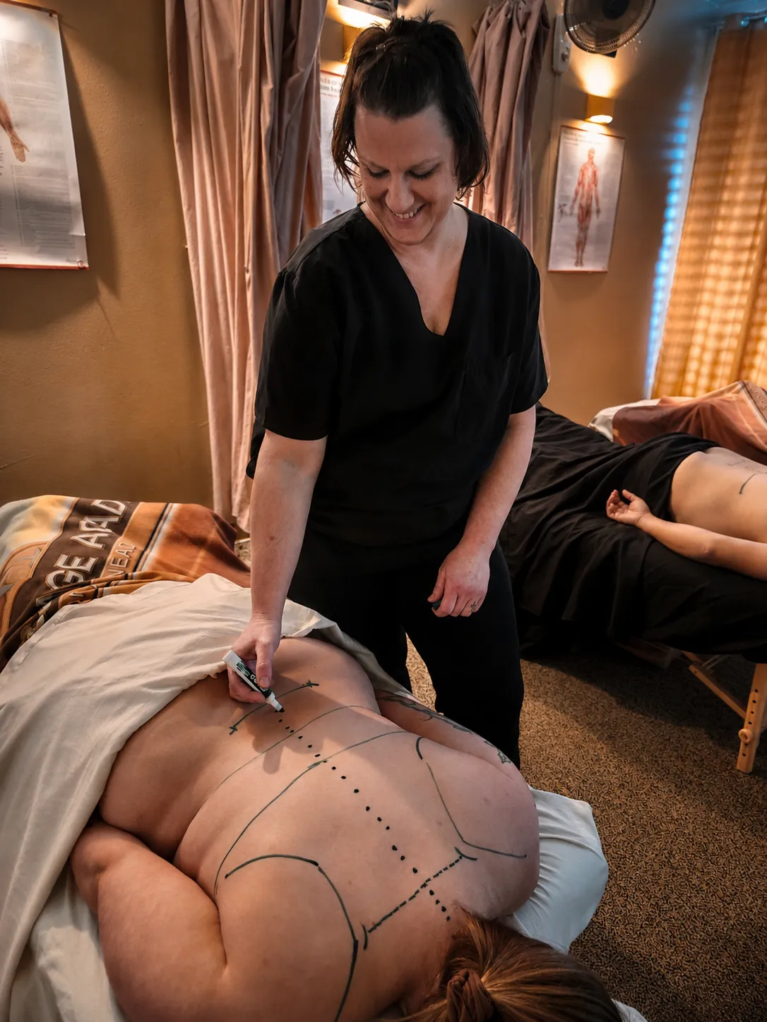 Smiling instructor drawing spinal lines on a client's back during class