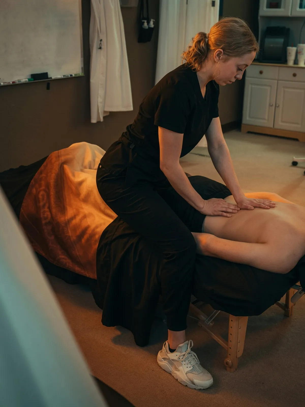 Student leaning into a client's back massage in a warmly lit treatment room