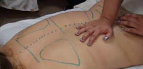 Person giving a massage in massage school and using anatomy with marker
